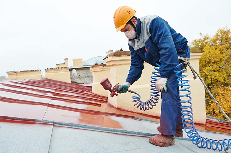 A contractor painting a metal roof with a commercial spray gun